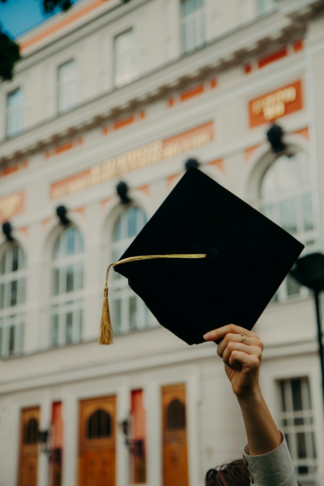Graduate holding cap in front of university representing the student pathway to permanent residency